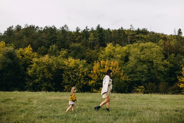 Foto zwangere vrouw en haar dochter lopen buiten in een veld met groen gras en brengen samen tijd door