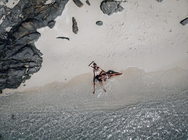 Zwangere vrouw en haar gelukkige echtgenoot liggend op het zand aan de pittoreske kust, drone-opname. Toekomstige ouders concept