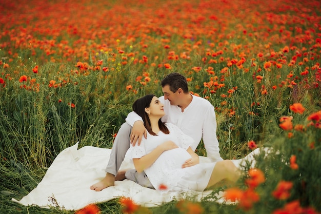 zwangere vrouw en haar man liggend op witte plaid in rode papaver veld