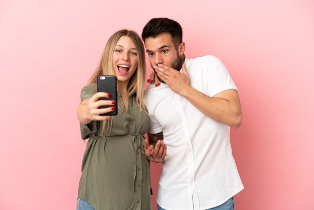 Zwangere vrouw en man over geïsoleerde roze achtergrond maken een selfie met de mobiel