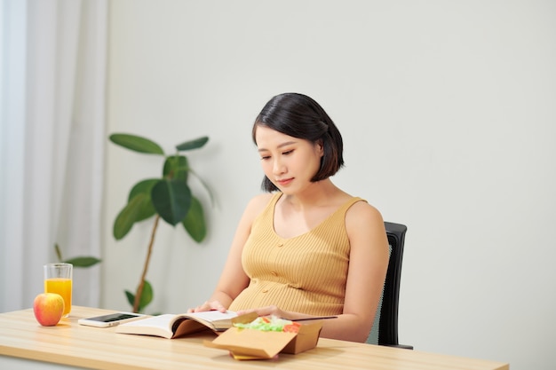 Zwangere vrouw gezond eten salade en tablet gebruiken terwijl u thuis ontspant.