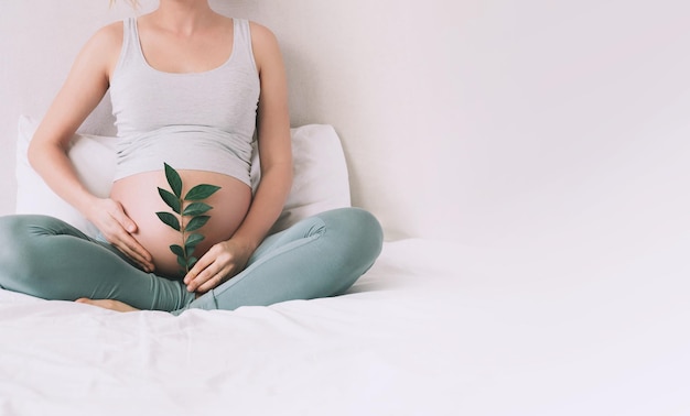 Zwangere vrouw houdt een groene spruit bij haar buik als symbool van nieuw leven welzijn vruchtbaarheid ongeboren baby gezondheid concept zwangerschap moederschap eco duurzame levensstijl gynaecologie