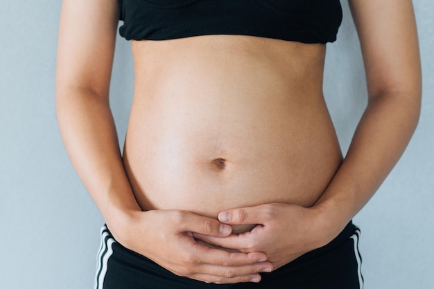 Zwangere vrouw houdt handen op buik en pastelkleurige achtergrond Zwangerschap moederschap voorbereiding en verwachting concept Close-up kopieerruimte Jonge vrouw wachten op babygeboorte