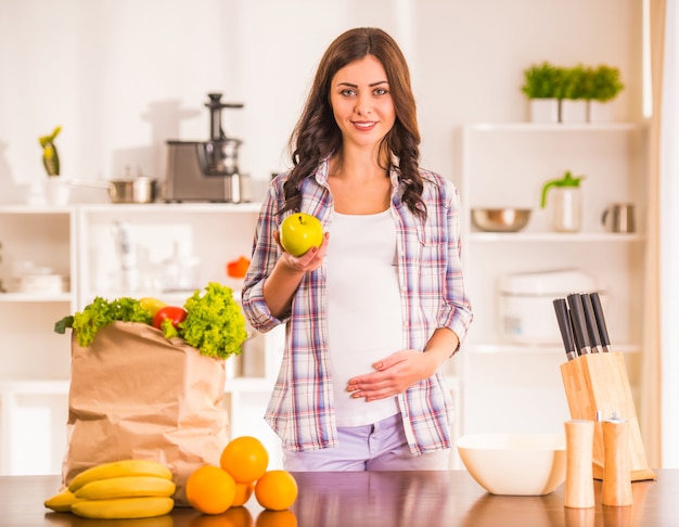 Zwangere vrouw in de keuken met groenten en fruit.