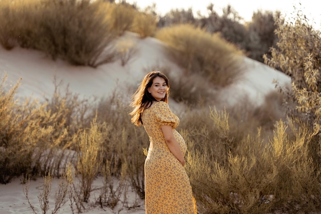 zwangere vrouw in een gele jurk op het strand is vrolijk
