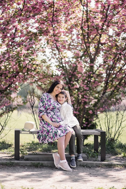 Zwangere vrouw in een jurk met haar zoon op een bankje in het park