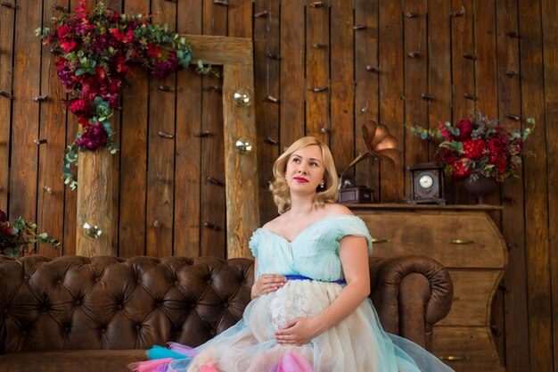 Foto zwangere vrouw in een kleurrijke gezwollen jurk op de muur van een houten interieur in een bloemenzolder. gelukkig zwangerschap