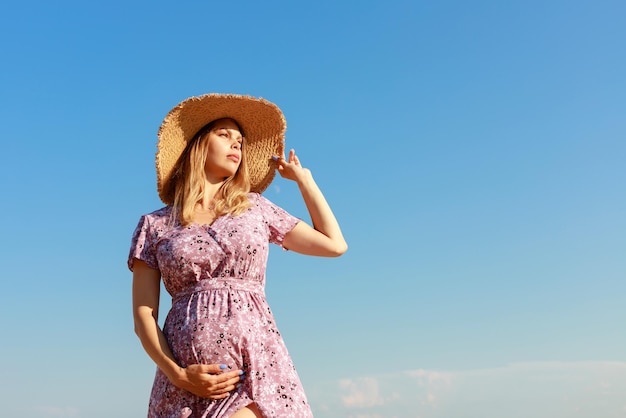 Zwangere vrouw in een strohoed op de blauwe hemel als achtergrond aan de zijkant
