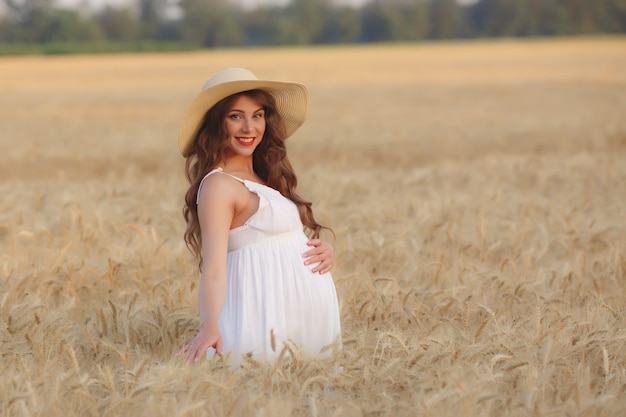 Zwangere vrouw in een strohoed op een gebied van tarwe