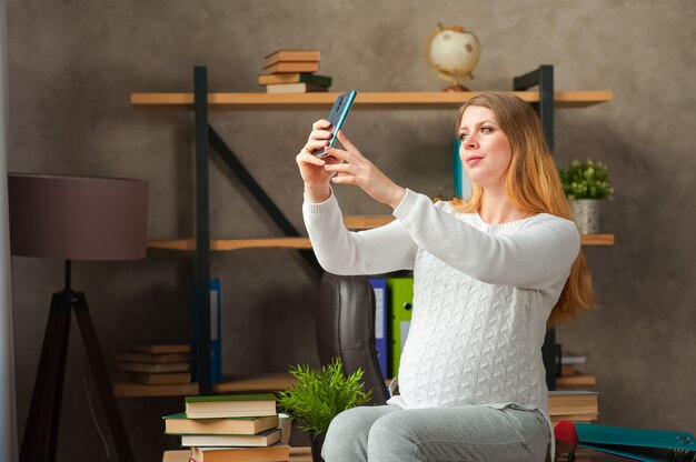 Zwangere vrouw in een witte trui. Zwangere blogger neemt selfie aan de telefoon.