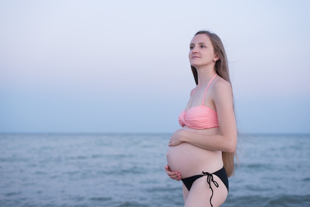 Zwangere vrouw in een zwempak op het strand.