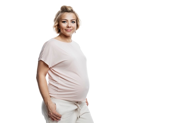 Zwangere vrouw in gezellige huiskleren. Een mooie glimlachende blondine in een licht T-shirt en broek.