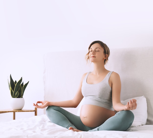zwangere vrouw in lotushouding die meditatie of ademhalingsoefeningen doet voor een gezonde zwangerschap