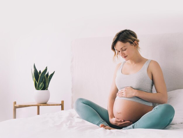 Zwangere vrouw in lotushouding die mediteert of ademhalingsoefeningen doet voor een gezonde zwangerschap en het lichaam voorbereidt op de bevalling Jonge aanstaande moeder die thuis yoga beoefent