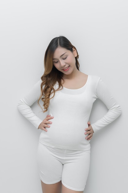 Zwangere vrouw in witte jurk gebruik handaanraking op haar buik op witte achtergrond Aziatische vrouwThailand mensen