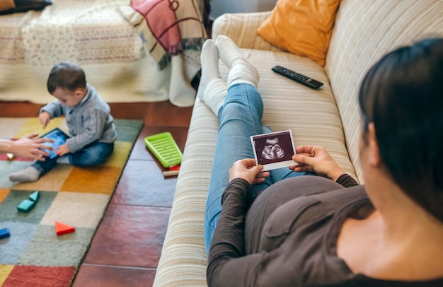 Zwangere vrouw kijkt naar de echo van haar nieuwe baby terwijl de oudere broer speelt