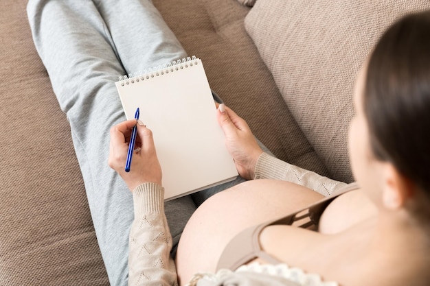 Zwangere vrouw maakt aantekeningen Concept van zwangerschap gezondheidszorg geneeskunde Moeder wacht op baby thuis