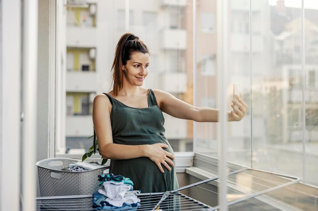 Zwangere vrouw maakt foto's aan de telefoon terwijl ze huishoudelijke klusjes doet