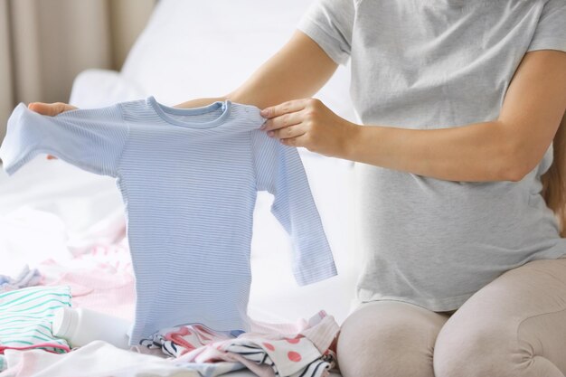 Zwangere vrouw met babykleertjes thuis