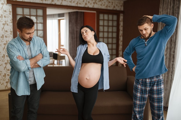 Zwangere vrouw met buik, twee mannen, wie is de vader, humor. Zwangerschap, prenatale periode thuis. Aanstaande moeder, grapje