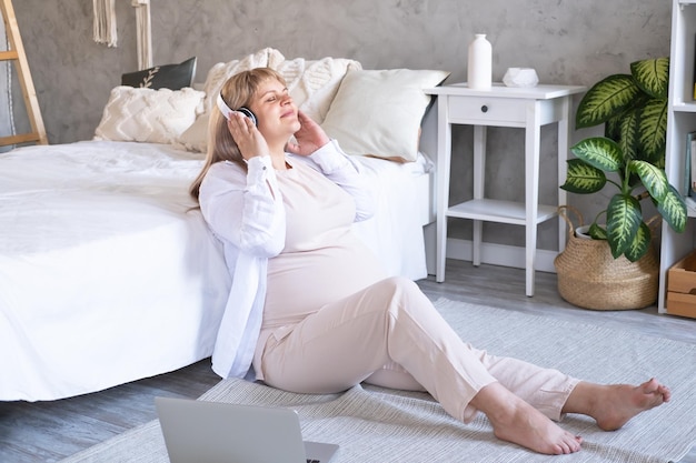 zwangere vrouw met dikke buik vergevorderde zwangerschap in draadloze hoofdtelefoon die muziek luistert