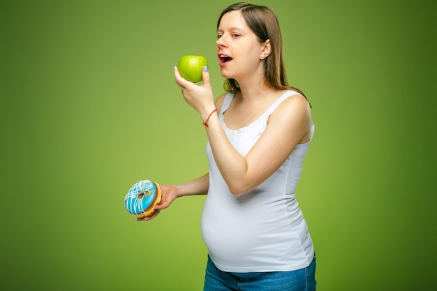 Zwangere vrouw met donut en groene appel advies welke producten je gezond moet eten