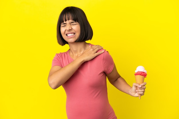 Zwangere vrouw met een cornet-ijs geïsoleerd op een gele achtergrond die lijdt aan pijn in de schouder omdat ze moeite heeft gedaan