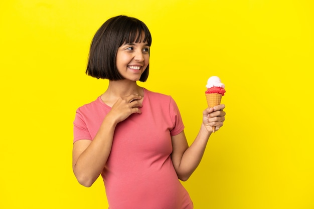 Zwangere vrouw met een cornet-ijs geïsoleerd op een gele achtergrond terwijl ze glimlacht