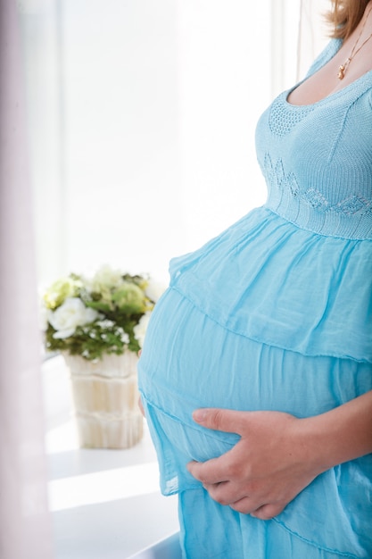 Zwangere vrouw met een dikke buik in de buurt van het venster close-up. vrouw zorgvuldig streelde haar zwangere buik binnen. vrouw in afwachting van de geboorte van een kind. 9 maanden gezonde zwangerschap en moederschap.