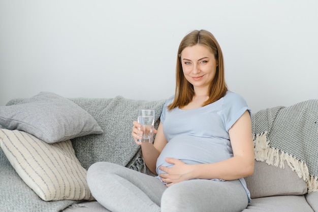 Zwangere vrouw met een glas water zittend op de bank in de kamer