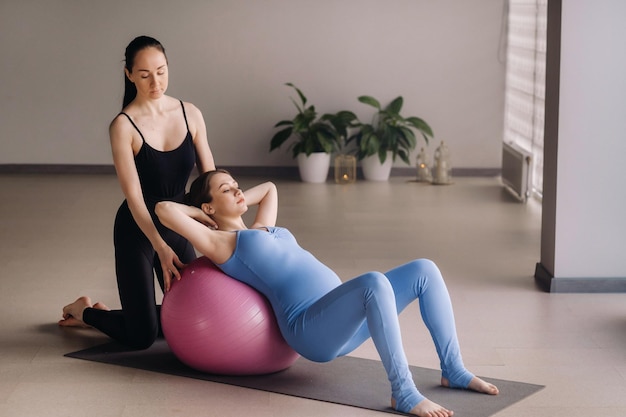 Zwangere vrouw met een trainer tijdens fitnesslessen met een bal