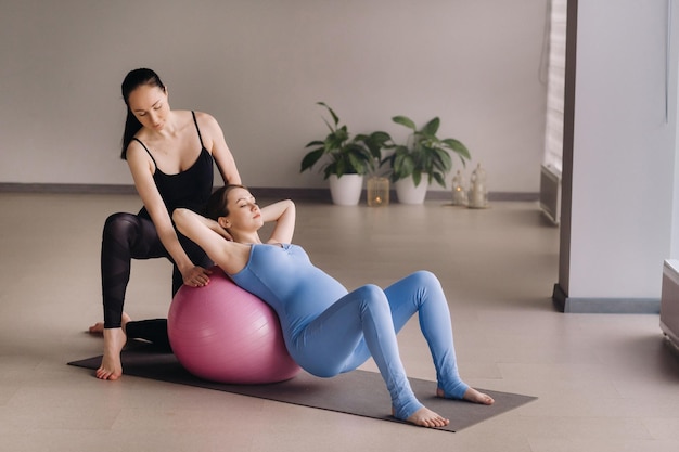 Zwangere vrouw met een trainer tijdens fitnesslessen met een bal
