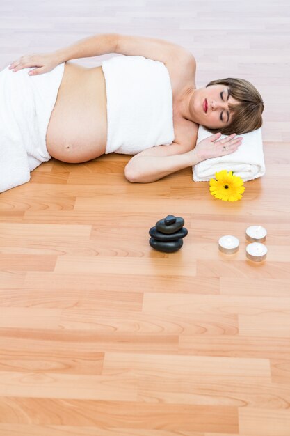 Zwangere vrouw met gesloten ogen het rusten op hardhoutvloer bij kuuroord