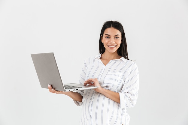zwangere vrouw met grote buik glimlachend en laptop in handen te houden terwijl je geïsoleerd over witte muur