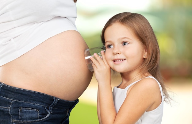 Zwangere vrouw met haar dochter die naar de baby in buik luistert