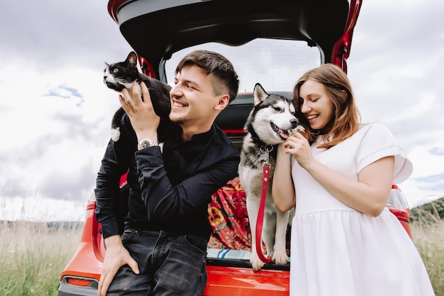 Zwangere vrouw met husky en kat op de schouders van de man in de buurt van auto in auto op natuurachtergrond