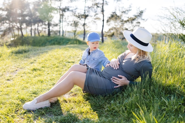 Zwangere vrouw met kind buitenshuis Moeder en haar zoon op de natuur in het voorjaarsbos Kleine jongen en moeder die voor de tweede keer zwanger zijn en tijd samen doorbrengen