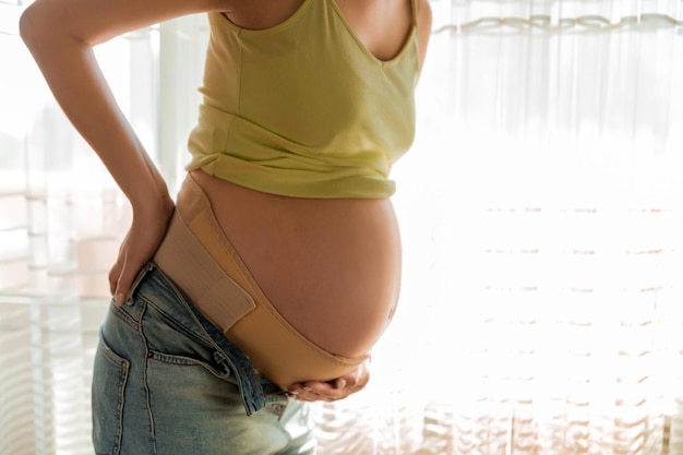 zwangere vrouw met orthopedische steungordel tegen rugpijn bij zwangere vrouw zonder raam Orthopedische ondersteuningsgordelconcept