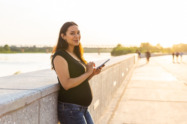 Zwangere vrouw met smartphone buitenshuis. Zwangerschap, technologie en communicatieconcept