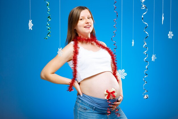 Foto zwangere vrouw met sneeuwvlokken op een blauwe achtergrond en rode slinger verwacht een baby met kerstmis