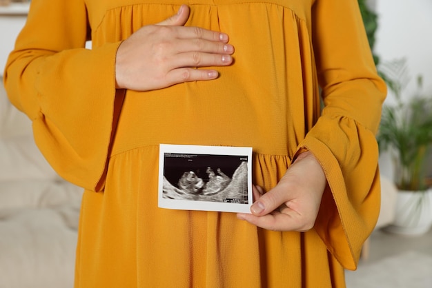 Zwangere vrouw met ultrasone klankbeeld van baby in woonkamerclose-up