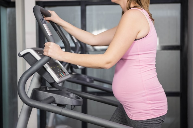 Zwangere vrouw op crosstrainer bij de gymnastiek