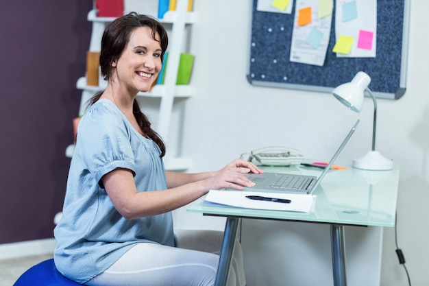 Zwangere vrouw op oefeningsbal die laptop met behulp van