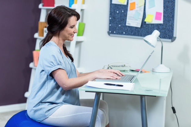 Zwangere vrouw op oefeningsbal die laptop met behulp van