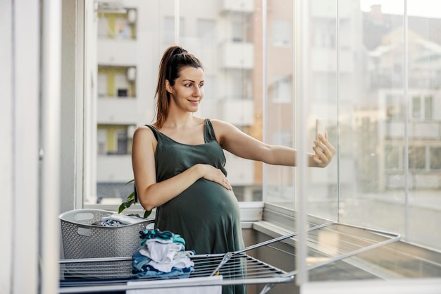 Zwangere vrouw poseert en maakt foto's aan de telefoon terwijl ze huishoudelijke klusjes doet