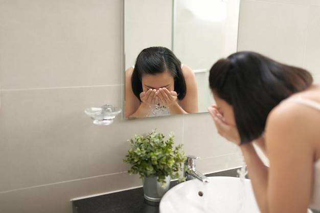 Zwangere vrouw spatten gezicht met water boven de wastafel in de badkamer