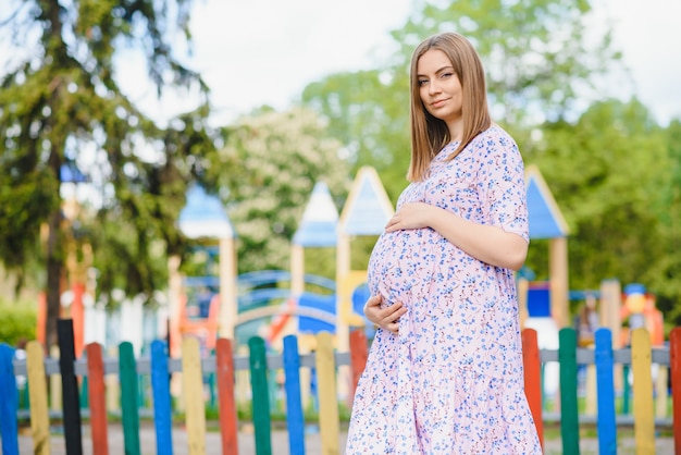 Zwangere vrouw staat in het park bij de speeltuin waar kinderen spelen.