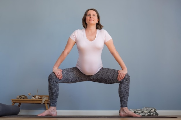 Zwangere vrouw staat in Sumo Squat oefening Godin pose Mooie vrouw beoefent thuis yoga
