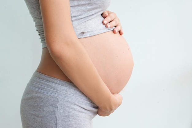 Zwangere vrouw staat zijwaarts en houdt haar buik vast. Zwangerschap, bevalling, moederschap.