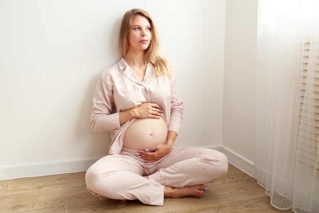 Zwangere vrouw streelt haar buik terwijl ze op de grond zit thuis moederschap concept